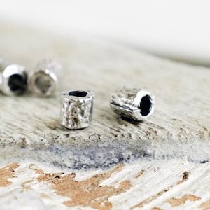 May include: Close-up of silver metal beads with a textured surface. The beads are round and have a hole in the center.