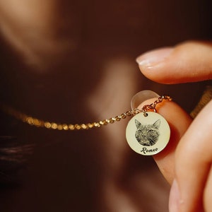 Puede incluir: Un collar de cadena dorada con un colgante redondo que presenta una foto en blanco y negro de la cara de un gato y el nombre "Romeo" grabado debajo.
