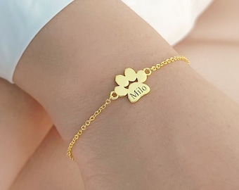 May include: Gold paw print charm bracelet with the name "Milo" engraved on the charm.