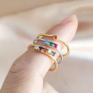 May include: Set of four gold rings with colorful gemstones. Each ring features a different colored gemstone, including red, green, blue, and purple.