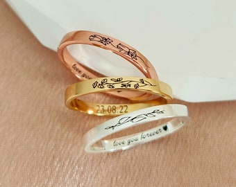 May include: Three thin gold, silver, and rose gold rings with engraved designs. The gold ring has the date "23.08.22" engraved on it. The silver ring has the words "love you forever" engraved on it. The rose gold ring has a floral design engraved on it.