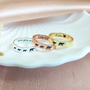 May include: Three personalised rings with a line of bear silhouettes. The rings are silver, rose gold, and gold. The silver ring says "love you mom", the rose gold ring says "Katie-Ellie", and the gold ring says "Katie" with a heart.