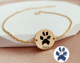 May include: Gold chain bracelet with a round charm featuring a black paw print and the name "OzZy" engraved below.