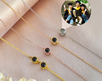 Puede incluir: Cuatro collares de plata, oro y oro rosa con cuentas negras. Cada collar tiene un pequeño dije de vidrio transparente que se puede usar para mostrar una foto. La foto muestra a tres personas con batas de graduación.