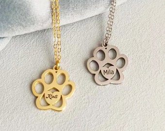 May include: Two gold and silver necklaces with paw print pendants. The gold pendant has the name "Kali" engraved inside the heart and the silver pendant has the name "Mila" engraved inside the heart.