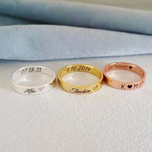 May include: Three personalized rings with engraved text and heart symbols. The rings are silver, gold, and rose gold.