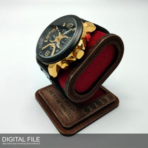 Peut inclure: Une montre-bracelet noire et dorée repose sur un présentoir en bois avec un coussin en velours rouge. Le présentoir porte la citation "TIME DOESN'T LIKE TO BE WASTED". La montre a un cadran noir et des détails dorés.