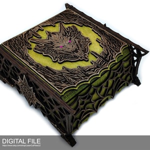 Puede incluir: Una caja de madera con un diseño verde y marrón. La parte superior de la caja presenta una talla detallada de una criatura con ojos rojos brillantes. La caja está decorada con un patrón de telaraña.