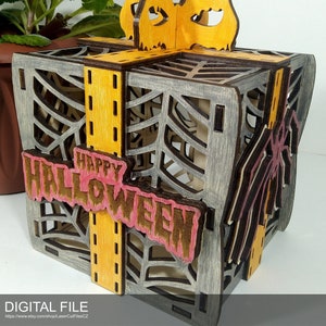Puede incluir: Una caja de madera con forma de caja de regalo con un diseño de telaraña y las palabras "Happy Halloween" en la parte delantera. La caja está decorada con una cinta amarilla y una araña en el lateral.