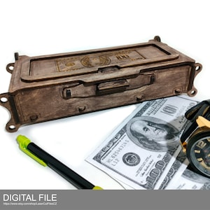 Puede incluir: Una caja de madera con diseño de maleta, con una imagen grabada con láser de un billete de 100 $. La caja es marrón y tiene una tapa con bisagras. La caja está sobre una superficie blanca con un bolígrafo y un reloj.