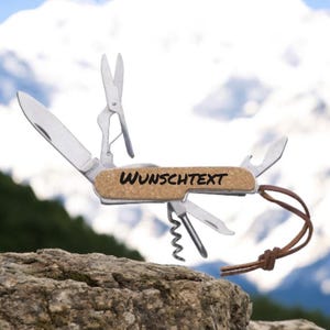 Könnte beinhalten: Ein Multifunktions-Taschenmesser mit einem Korkgriff. Der Griff trägt den Text "WUNSCHTEXT". Das Messer verfügt über eine Vielzahl von Werkzeugen, darunter eine Klinge, einen Flaschenöffner, einen Korkenzieher und eine Schere.