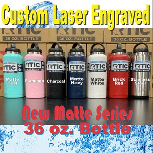 May include: A set of eight 36-ounce RTIC insulated water bottles in various matte colors, including teal, flamingo, charcoal, navy, white, brick red, and stainless steel. The bottles are arranged in a row on a table with their corresponding color names displayed below each bottle. The text "New Matte Series 36 oz. Bottle" is displayed below the bottles.