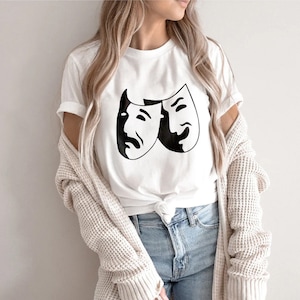 May include: White t-shirt with a black graphic of two theatrical masks, one smiling and one frowning.