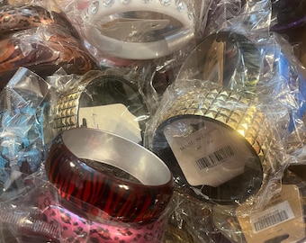 May include: A collection of various bangles in clear plastic packaging. The bangles are in different colors and designs, including white with rhinestones, gold with studs, and red with black stripes. Other bangles have leopard print patterns.