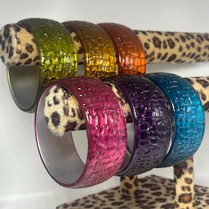 May include: Set of six colorful plastic bangles with a crocodile skin texture. The bangles are in shades of green, orange, pink, purple, and blue.