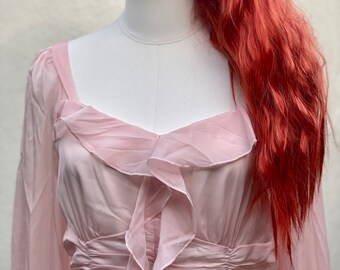 May include: A pink, long-sleeved, sheer dress with a ruffled neckline and a cinched waist.