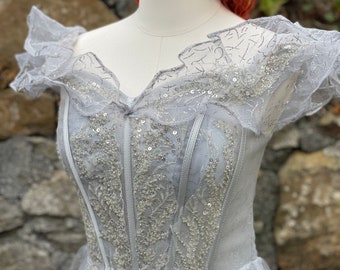 May include: A light blue tulle dress with a lace bodice and silver sequins. The dress has a sweetheart neckline and short sleeves.