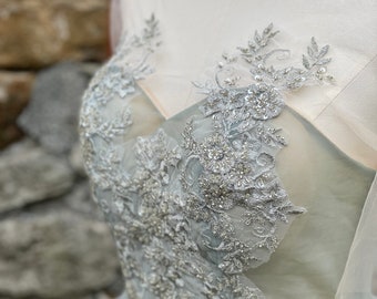 May include: A light blue tulle dress with silver lace and bead embellishments. The dress has a sweetheart neckline and a fitted bodice.