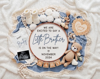 Op de afbeelding: Een blauwe en witte baby-aankondiging met een houten bord waarop staat "We are excited to say a little brother is on the way! November 2024". Het bord is omringd door een wit rompertje, een teddybeer, houten blokken die "baby" spellen en een houten hart waarop "Coming Soon" staat.