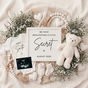 May include: A baby announcement featuring a white onesie with "Baby Smith" printed on it, a letter board with the text "We have been keeping a little secret", a teddy bear, and a sonogram image. The announcement is surrounded by greenery and decorative elements.