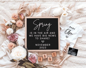 Op de afbeelding: Een zwangerschapsaankondiging met een zwart letterbord met de tekst "Spring is in the air and we have big news to share!" en "November 2023". Bevat een witte romper met "Baby Olsen", babyschoentjes, houten blokken en een echo, op een getextureerd oppervlak.