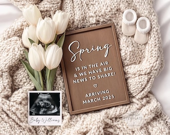 Pode incluir: Uma placa de madeira com o texto "Spring is in the air & we have big news to share!" e "Arriving March 2025". A placa é cercada por tulipas brancas, uma imagem de ultrassom de bebê e um par de sapatinhos de bebê.