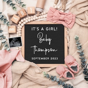 May include: A baby announcement flat lay featuring a black letter board with the text "IT'S A GIRL! Baby Thompson September 2023." The image includes pink baby shoes, a pink headband, wooden blocks, and a sonogram.