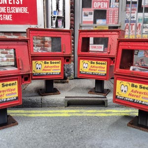 Może przedstawiać: Cztery czerwone, zabytkowe automaty do sprzedaży gazet ze szklanymi oknami i czarnymi podstawami. Każda maszyna ma żółty znak z napisem "Be Seen! Advertise Here!" i numerem telefonu. Tło obejmuje ceglaną ścianę i witrynę sklepową.
