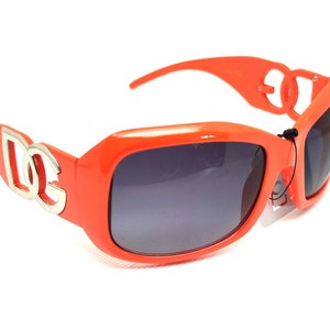 May include: Orange sunglasses with a silver logo on the side. The logo is the letters "DG" in a stylized font.