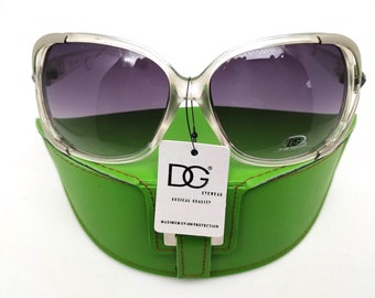 May include: Clear framed sunglasses with dark gray lenses, resting in a green case with a brown leather trim. The case has a white tag with the text "DG EYEWEAR OPTICAL QUALITY MAXIMUM UV PROTECTION".