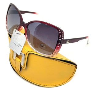 May include: Red and pink sunglasses with rhinestones around the frame and a yellow case. The sunglasses have a dark lens and the case has the text "EyeWear Optical Quality" on a tag.