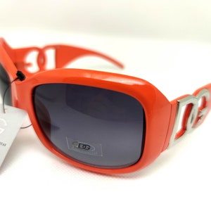 May include: Orange sunglasses with a silver DG logo on the side. The sunglasses have dark gray lenses.
