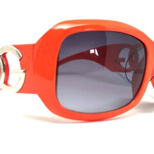 May include: Orange sunglasses with a silver DG logo on the side. The sunglasses have a dark gray lens.