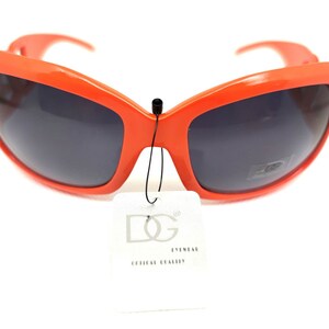 May include: Orange plastic sunglasses with dark lenses and a black tag that says "DG Eyewear Official Quality".