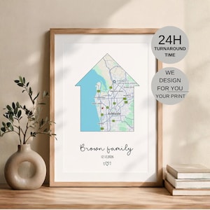 May include: A framed wall print featuring a house-shaped map of Adelaide, Australia. Below the map, the text reads Brown family, the date 12.12.2026, and a small heart icon. The print is displayed in a light wood frame on a flat surface.