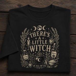 Könnte beinhalten: Ein schwarzes T-Shirt mit einem cremefarbenen Grafikdruck und dem Text "THERE'S A LITTLE WITCH IN ALL OF US." Das Design zeigt Illustrationen von einem Mond, einer Kerze, einem Kessel, einer Flasche mit "LAVENDER", einer "TEQUILA"-Flasche und Kräutern.