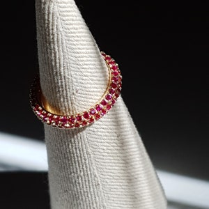 May include: A gold ring with a double row of red gemstones. The ring is displayed on a white fabric cone.