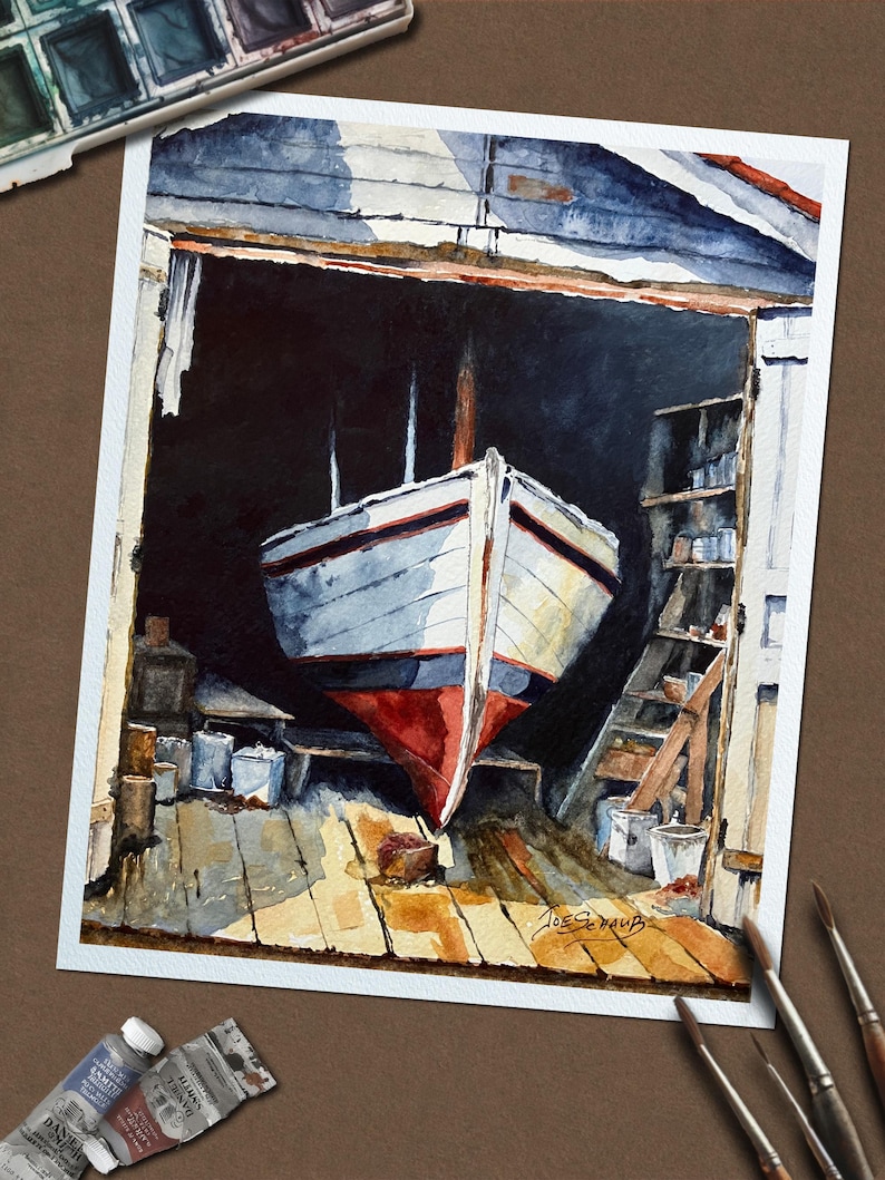 May include: A watercolor painting depicts a white boat with a red hull inside a dark wooden boat shed. The boat is positioned on a wooden floor with visible structural beams and shelves. The artist's signature, Joe Schaub, is visible in the corner.