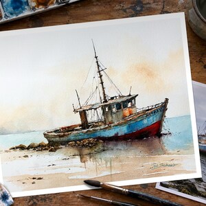 May include: A watercolor painting of a weathered fishing boat resting on a sandy shore. The vessel features a blue hull with a red lower section, a tall mast, and a cabin. The artist's signature, Joe Schaub, is visible in the bottom right corner.