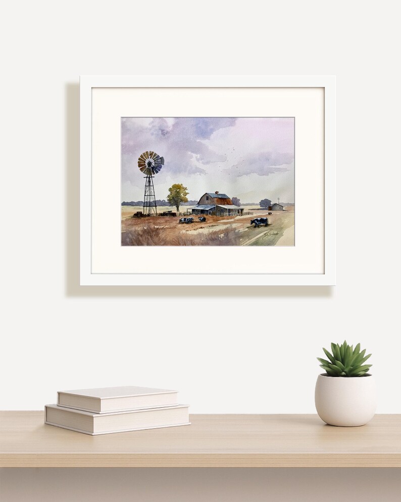 May include: Watercolor painting of a rural farm scene, framed in white. The artwork depicts a windmill, barn, and fields under a cloudy sky. The color palette includes muted tones of brown, blue, and purple, creating a serene landscape.