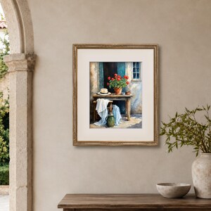 May include: A framed painting depicting a wooden table set against a wall with a window. On the table sits a terracotta pot filled with vibrant red flowers and a straw hat. A white cloth drapes over a stool, and a green ceramic pitcher sits below.