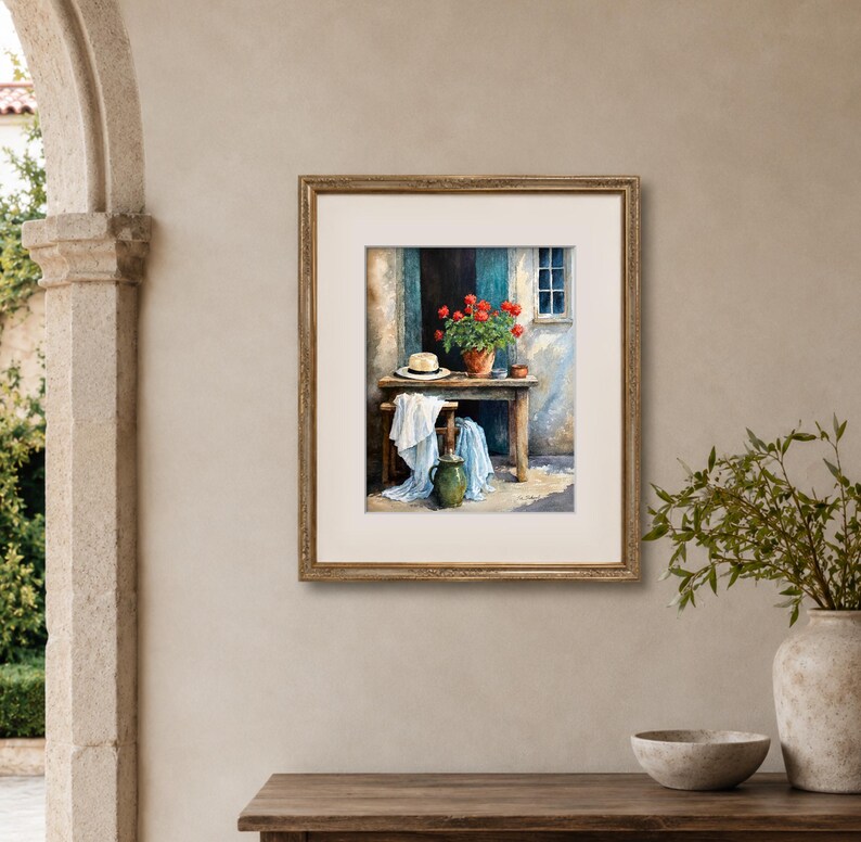 May include: A framed painting depicting a wooden table set against a wall with a window. On the table sits a terracotta pot filled with vibrant red flowers and a straw hat. A white cloth drapes over a stool, and a green ceramic pitcher sits below.