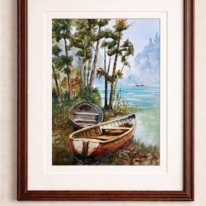 Op de afbeelding: Aquarel schilderij van een serene meer sc&egrave;ne met drie houten roeiboten aan de oever. De boten zijn bruin en rood, met bomen en een mistige berg op de achtergrond. Het kunstwerk is ingelijst in een donkerbruine houten lijst.