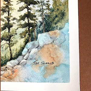 May include: Watercolor painting of a forest scene with tall evergreen trees and rocky terrain. The artwork features shades of green, blue, and brown. The artist's signature, "Joe Schaub," is visible in the lower right corner.
