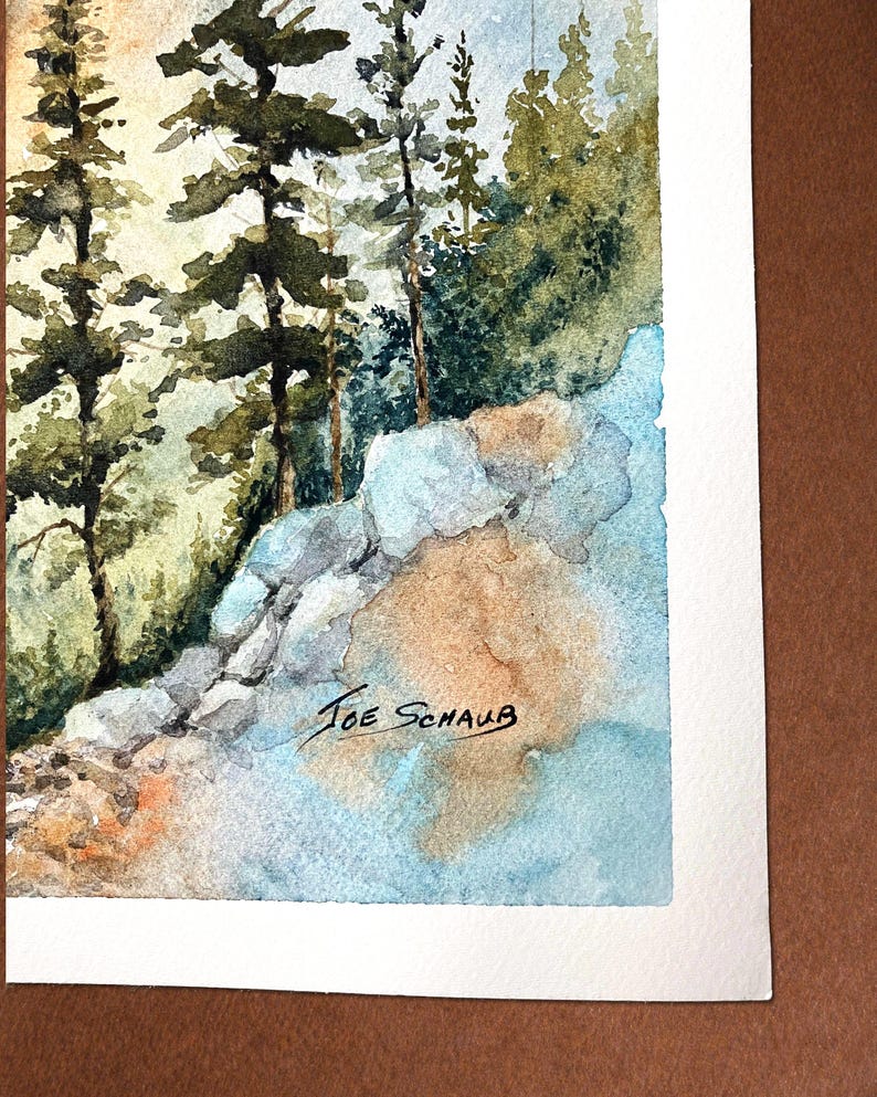 May include: Watercolor painting of a forest scene with tall evergreen trees and rocky terrain. The artwork features shades of green, blue, and brown. The artist's signature, "Joe Schaub," is visible in the lower right corner.