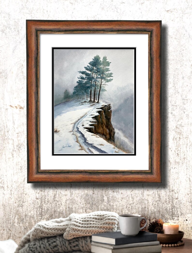 K&ouml;nnte beinhalten: Ein gerahmtes Aquarellgem&auml;lde zeigt eine schneebedeckte Klippe mit immergr&uuml;nen B&auml;umen. Das Kunstwerk ist in einem braunen Holzrahmen gefasst und schafft eine ruhige Landschaftsszene. Das Gem&auml;lde f&auml;ngt eine winterliche, nat&uuml;rliche Umgebung ein.