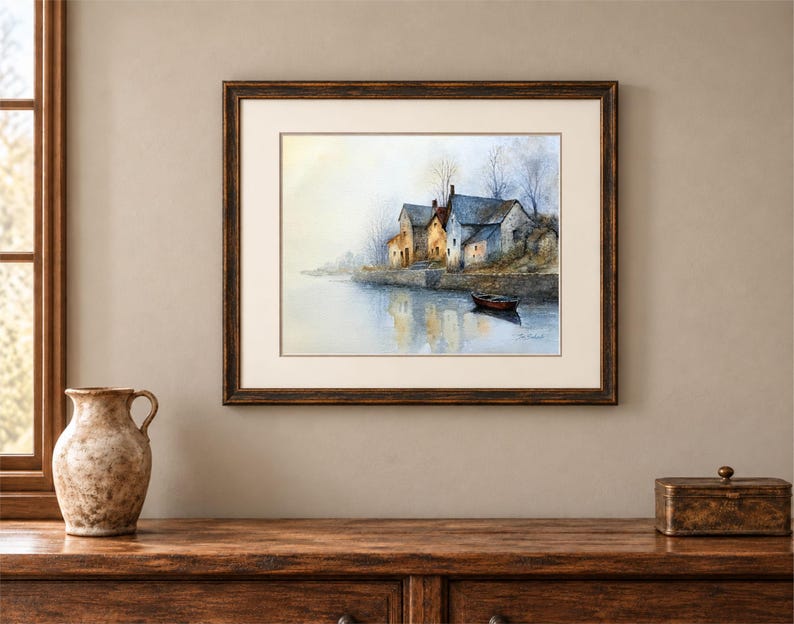 Puede incluir: Una pintura de acuarela enmarcada que representa un grupo de edificios de piedra a lo largo de una orilla tranquila con un peque&ntilde;o bote flotando en el agua. La escena presenta tonos suaves y apagados de azul, gris y amarillo c&aacute;lido.