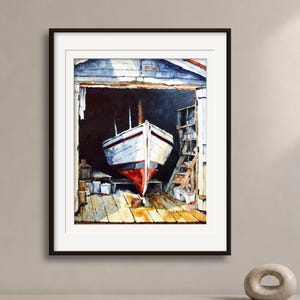 May include: A framed watercolor painting depicting a white boat with a red hull resting inside a dark wooden boathouse. The scene features a wooden floor, shelves with various items, and a signature in the bottom right corner of the artwork.