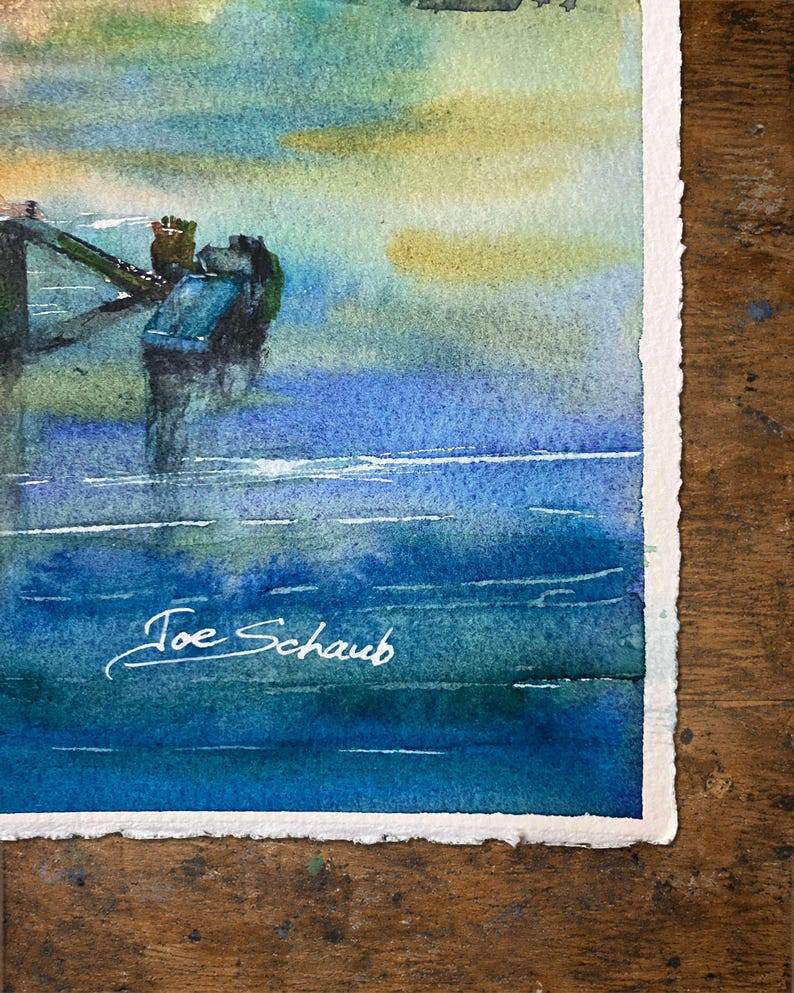 Puede incluir: Una pintura de acuarela sobre papel texturizado que muestra un paisaje marino azul y verde con una estructura de muelle oscura que se extiende hacia el agua. La obra presenta una firma en tinta blanca que dice Joe Schaub en la esquina inferior izquierda.