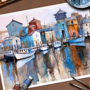 May include: Watercolor painting of a harbor scene with boats and buildings in shades of blue, orange, and white. The artwork features reflections in the water and is signed by the artist. Paint tubes and brushes are visible in the image.